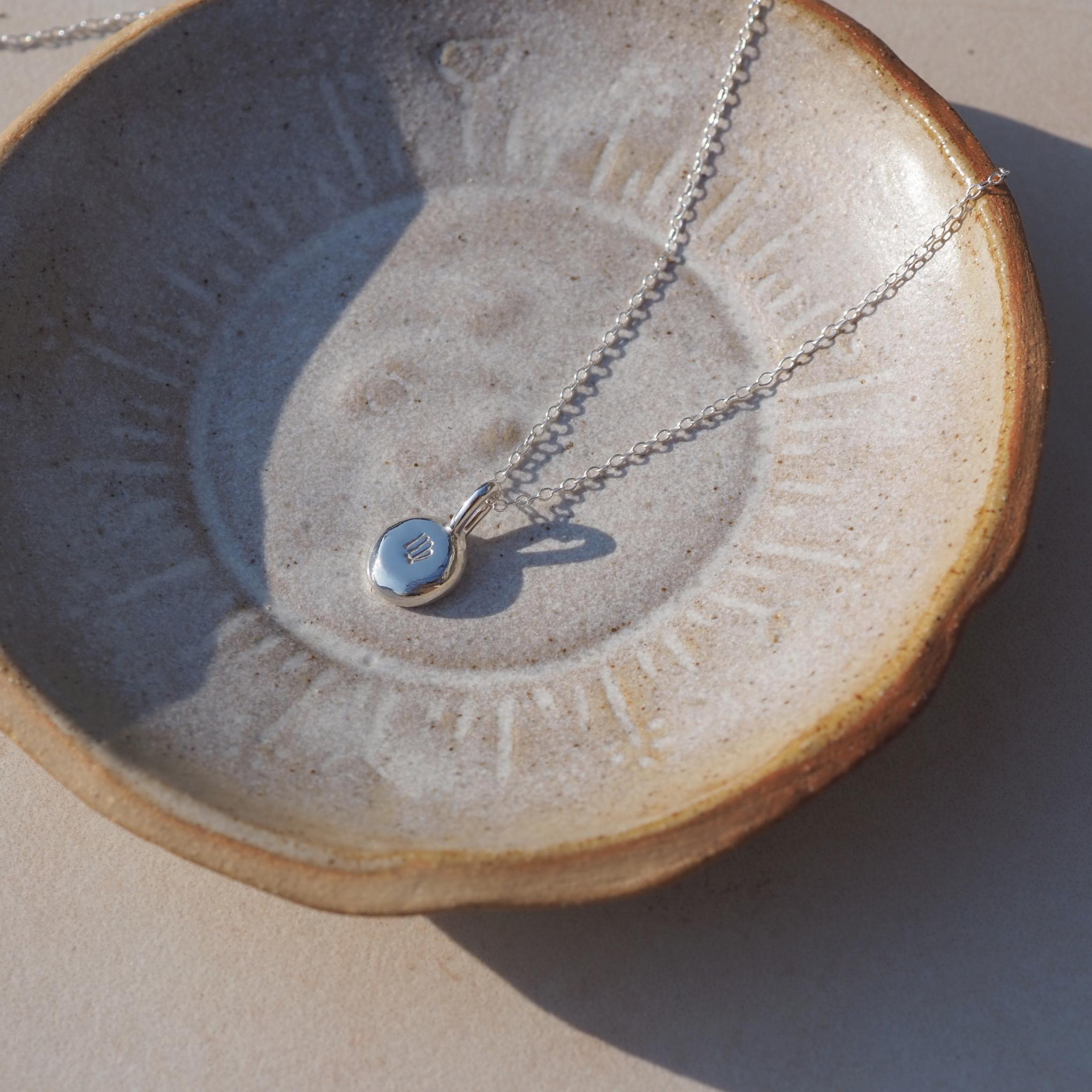 Personalised molten pebble necklace in sterling silver with hand-stamped zodiac sign