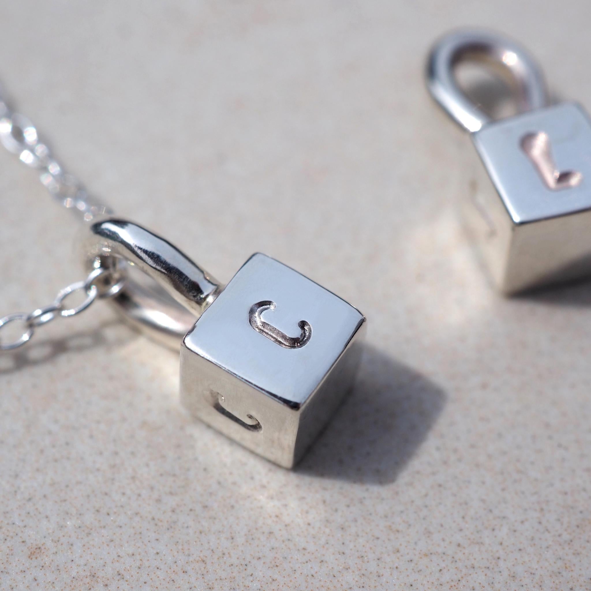 Close up of a hand-stamped initial on a dainty cube necklace