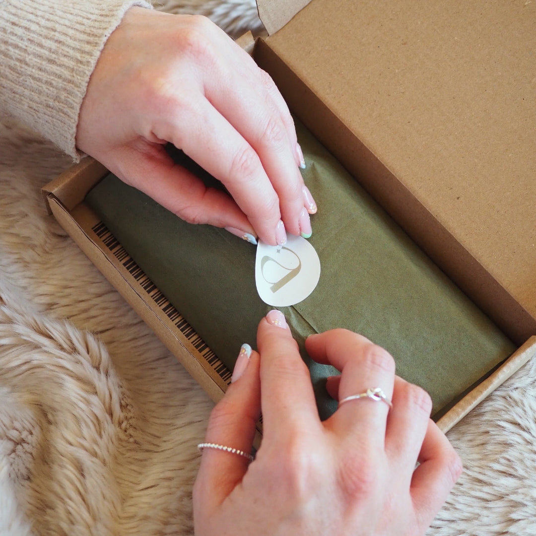 Hands unboxing personalised jewellery wrapped in eco-friendly green tissue paper