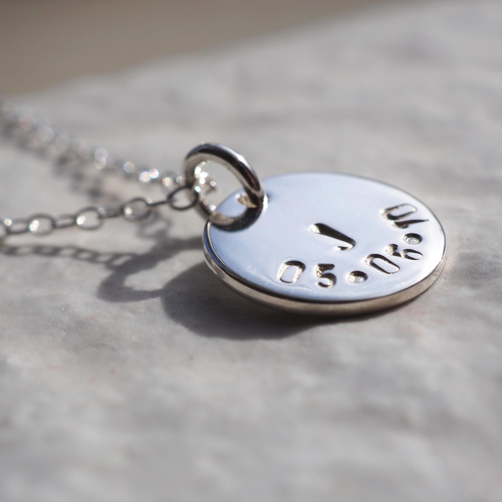 Close up of a hand-stamped initial and date disc necklace in sterling silver